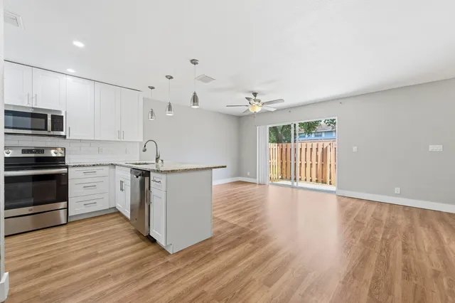 a kitchen with stainless steel appliances granite countertop a stove top oven a sink and white cabinets with wooden floor