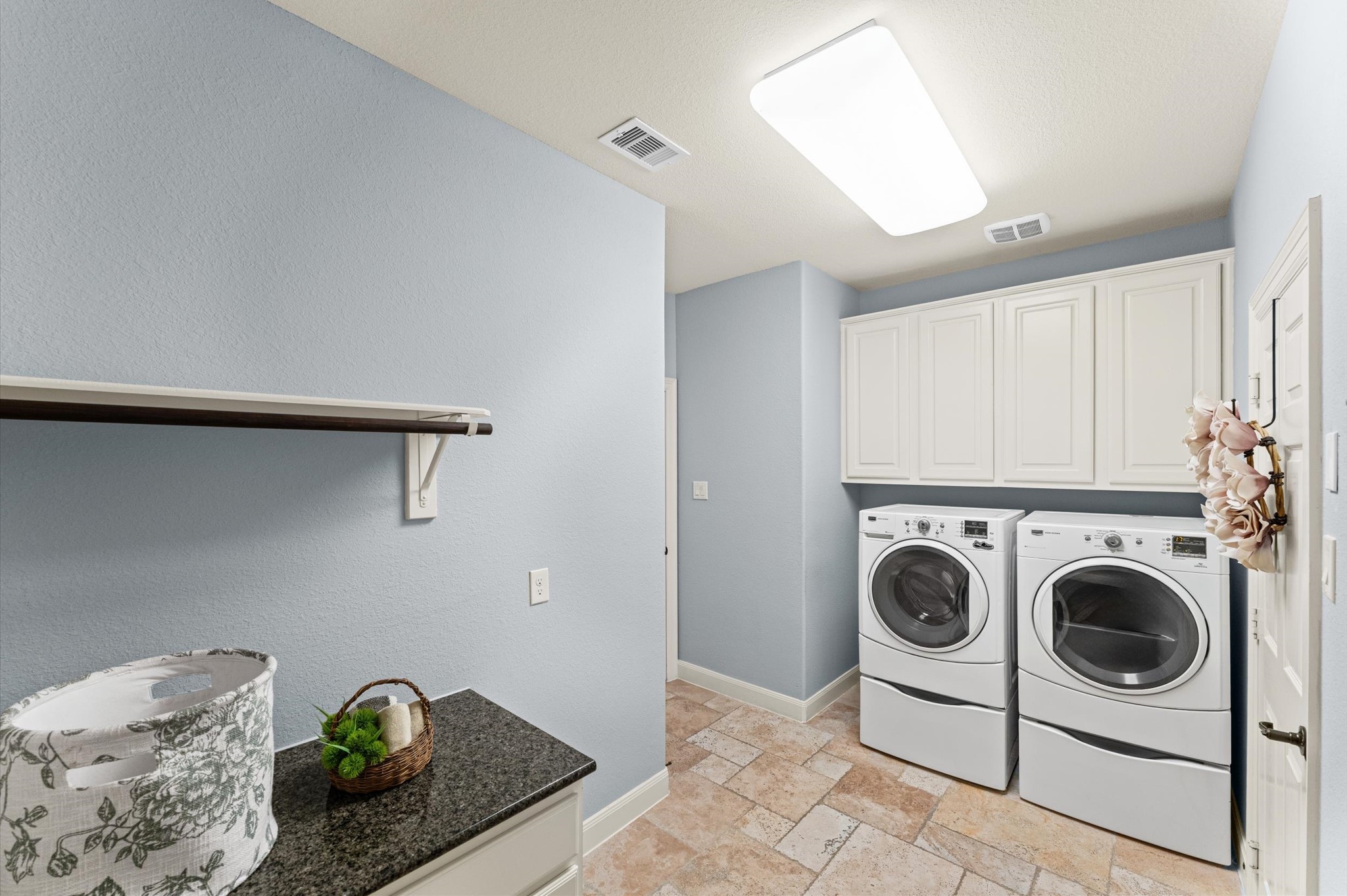 70 Valera Ridge Drive Spring, TX 77389 - Photo 32 of 37 This laundry room features a modern washer and dryer set, ample overhead cabinetry for storage, and a sleek countertop with a decorative basket. The room has a clean and bright design with light blue walls and tiled flooring.