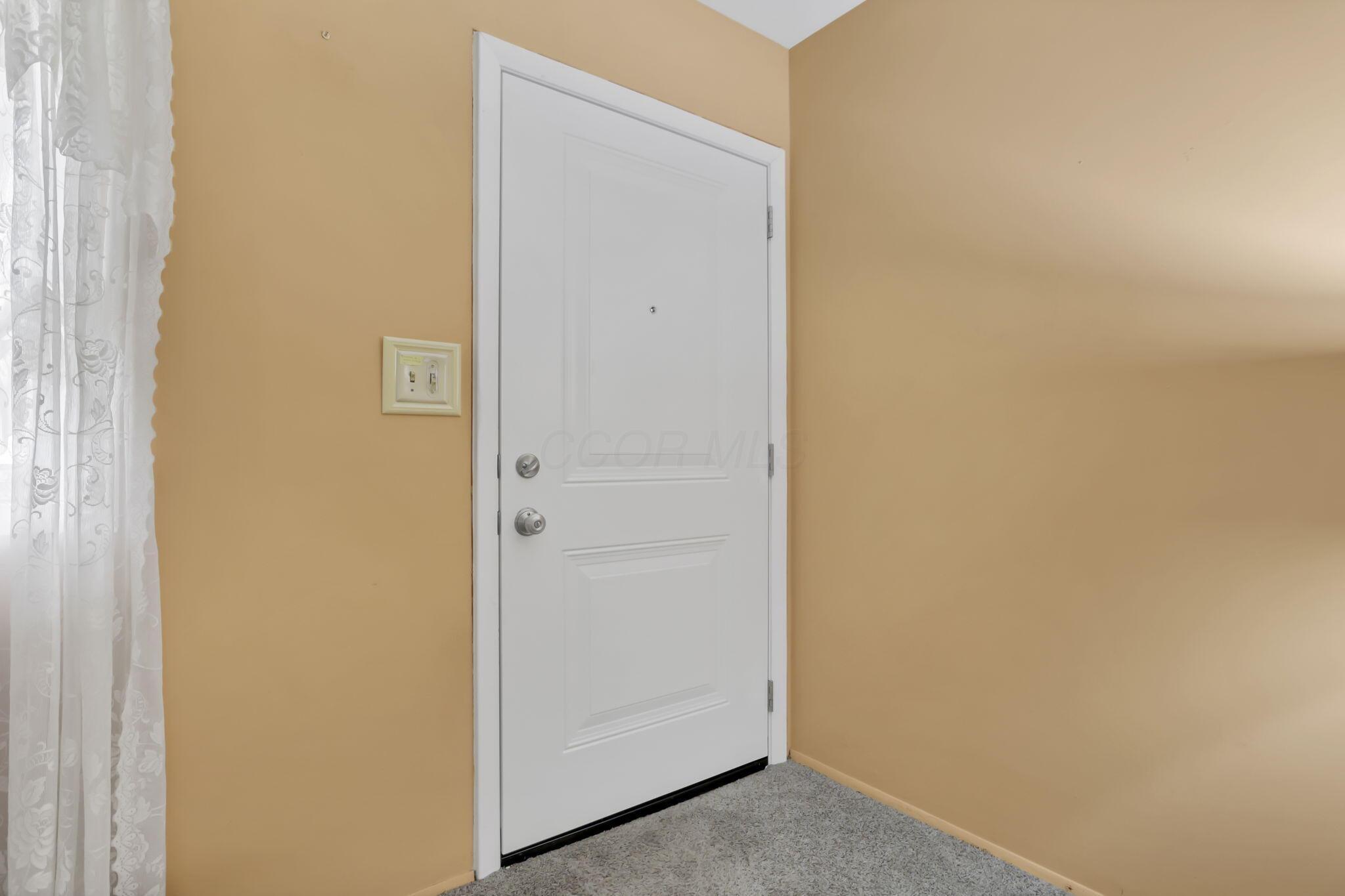 3882 Glenfield Road Columbus, OH 43232 - Photo 6 of 29 White interior door with panel detailing, set against warm-toned walls, featuring a light switch panel, chrome hardware, and gray carpeting