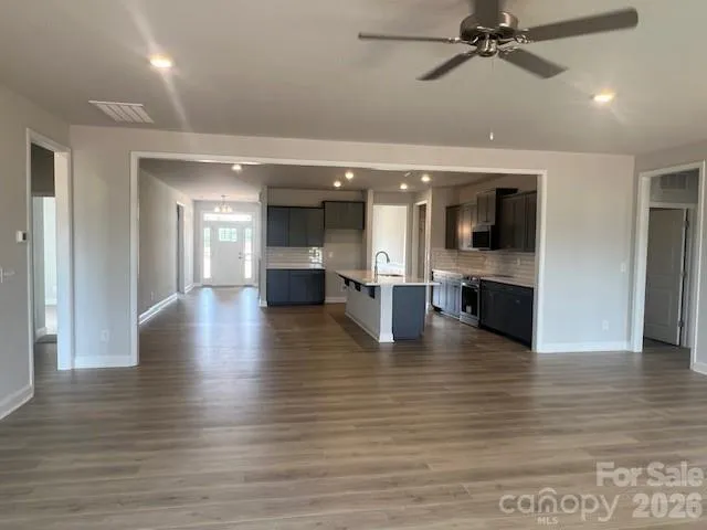 an empty room with wooden floor kitchen view and a window