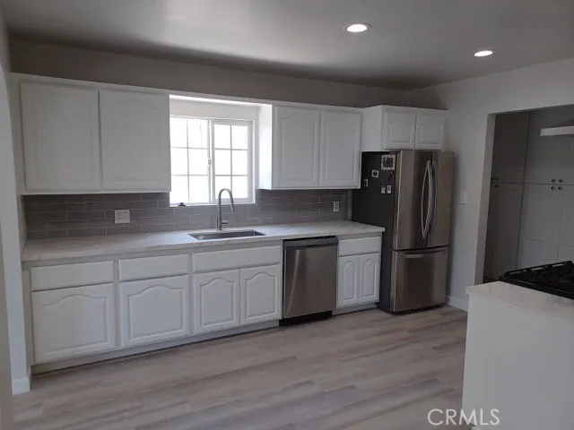 a kitchen with a refrigerator stove a sink and white cabinets with wooden floor