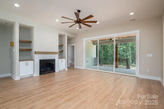 a view of an empty room with wooden floor fireplace and a window