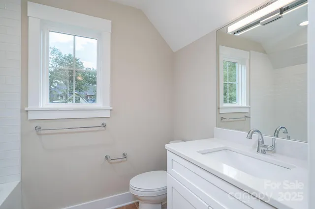 a bathroom with a granite countertop toilet a sink a mirror and a window