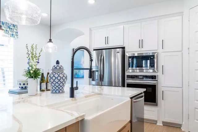 a kitchen with stainless steel appliances kitchen island granite countertop a refrigerator a stove and white cabinets with wooden floor