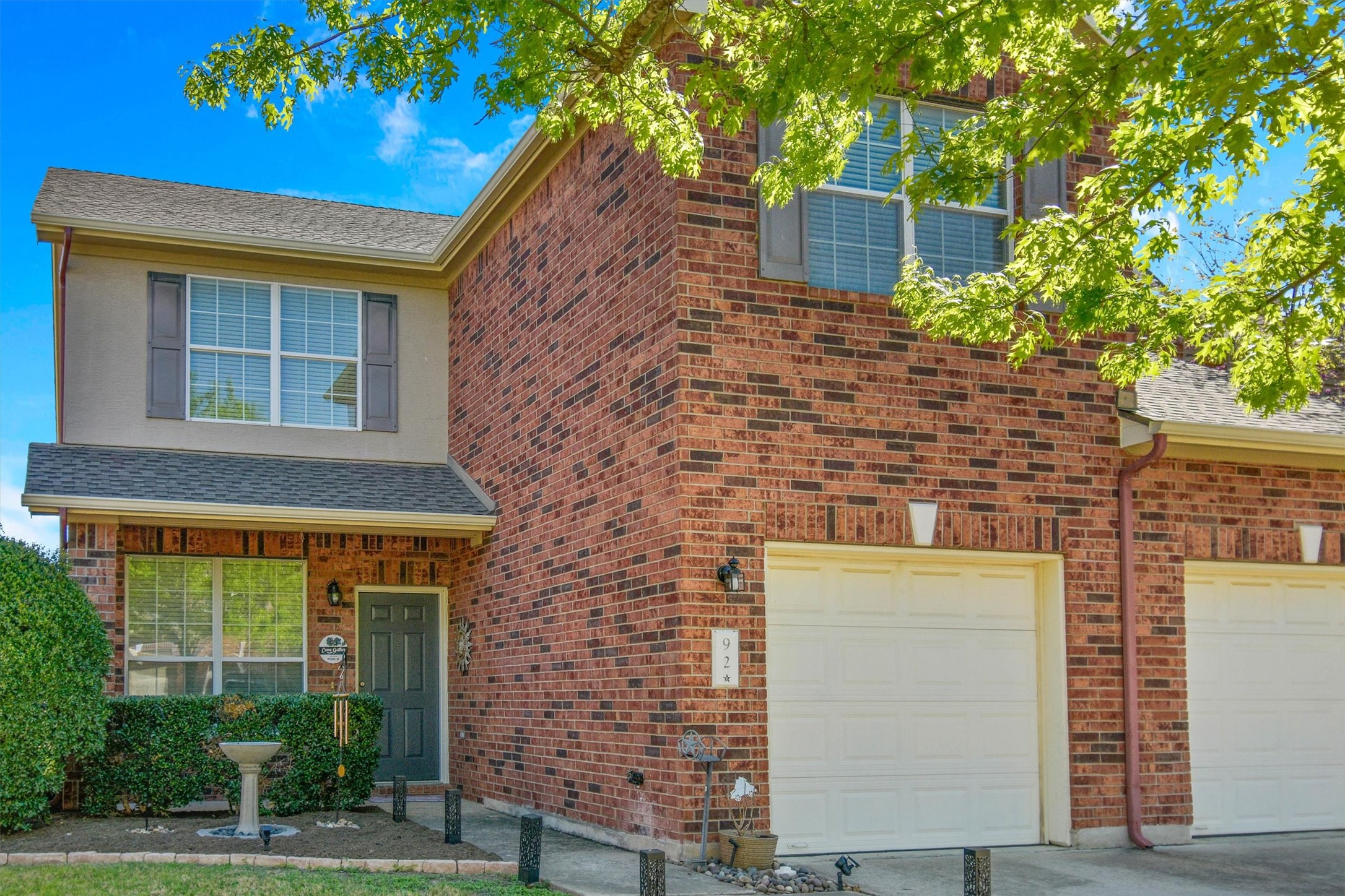 Traditional-style home featuring roof with shingles, brick siding, a porch, and an attached garage
