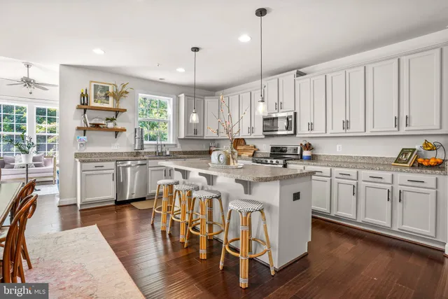 a kitchen with stainless steel appliances granite countertop white cabinets a stove a sink and a chairs