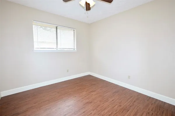 an empty room with wooden floor chandelier fan and windows