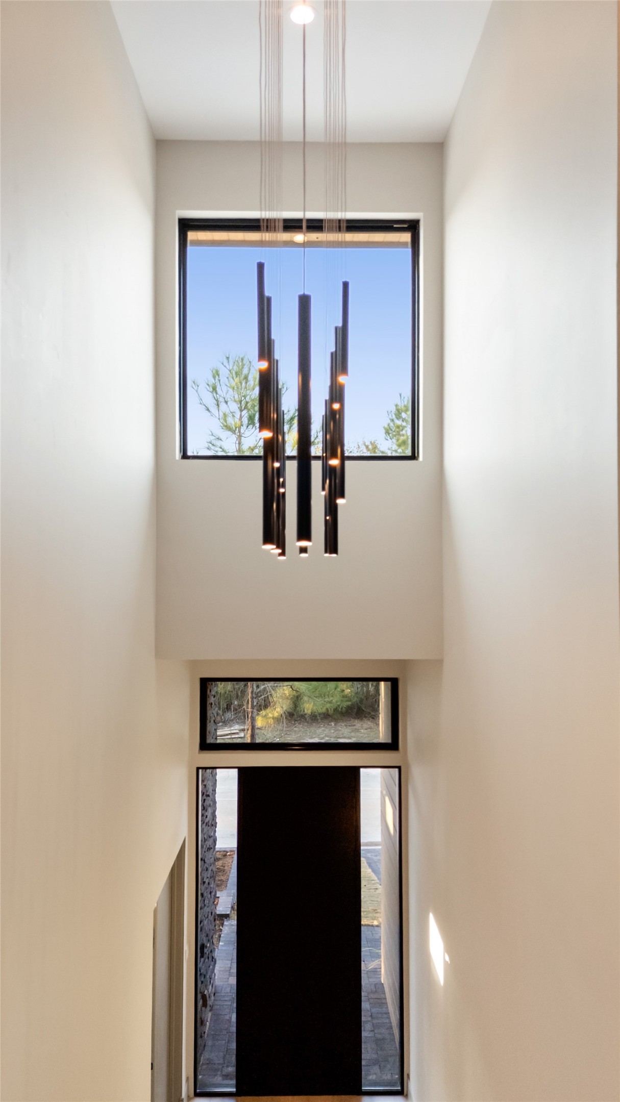 47 Pronghorn Place Spring, TX 77389 - Photo 2 of 44 The photo showcases a modern entryway with high ceilings and a large window above the door, allowing natural light to fill the space. A stylish, contemporary chandelier adds elegance to the minimalist design.