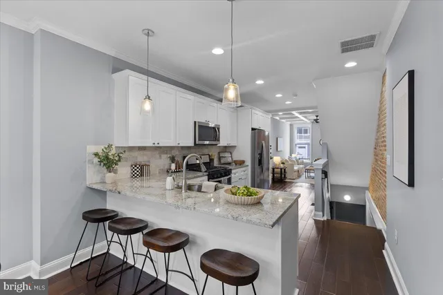 a kitchen with stainless steel appliances kitchen island granite countertop a dining table chairs and a refrigerator
