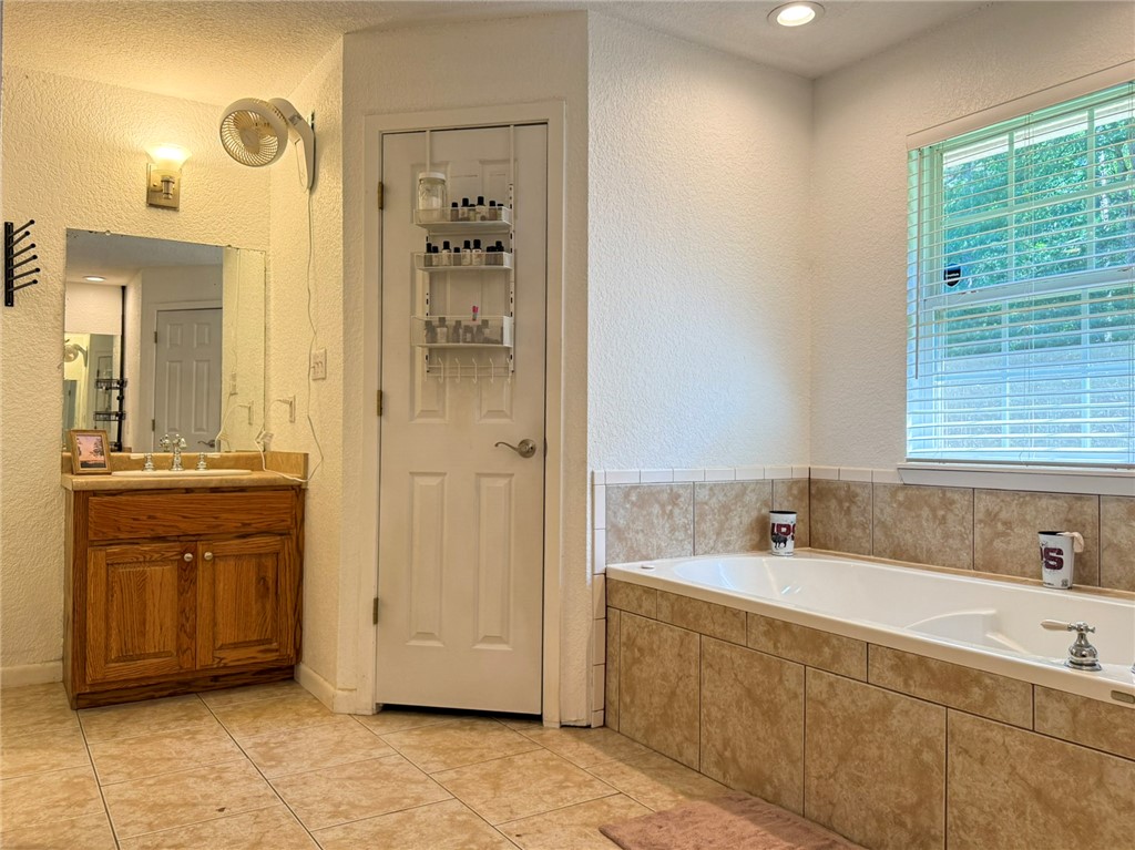 70 Walthall Road Russellville, AR 72802 - Photo 30 of 51 Primary Bathroom featuring a built-in soaking tub with a tiled surround, a wood-finish vanity with a single sink and wall-mounted mirror, and tile flooring