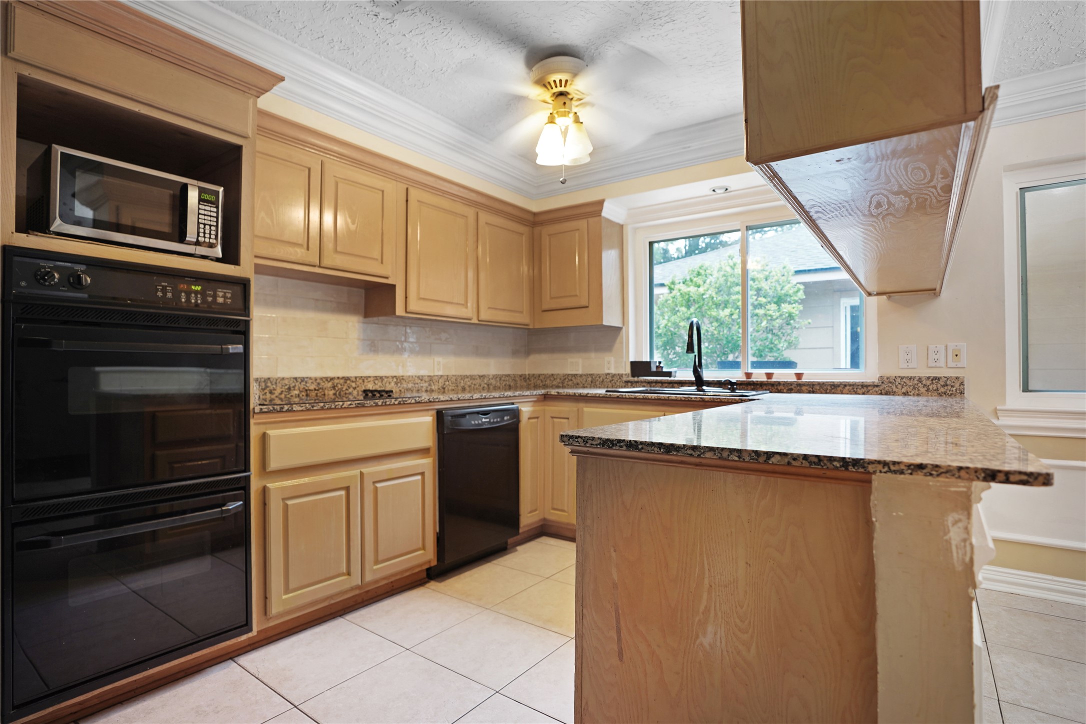 17119 Mellow Ridge Drive Spring, TX 77379 - Photo 13 of 32 This kitchen features warm wood cabinetry, granite countertops, and a modern appliance suite including a built-in microwave and double oven. A large window provides natural light, and a ceiling fan adds comfort.