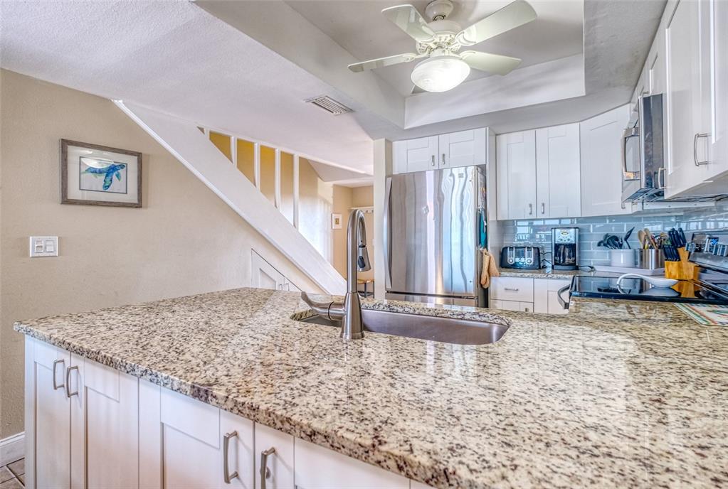 60 Gulf Boulevard, Unit 204 Indian Rocks Beach, FL 33785 - Photo 9 of 45 a view of a kitchen with kitchen island granite countertop a refrigerator a stove a sink a dining table and chairs with wooden floor