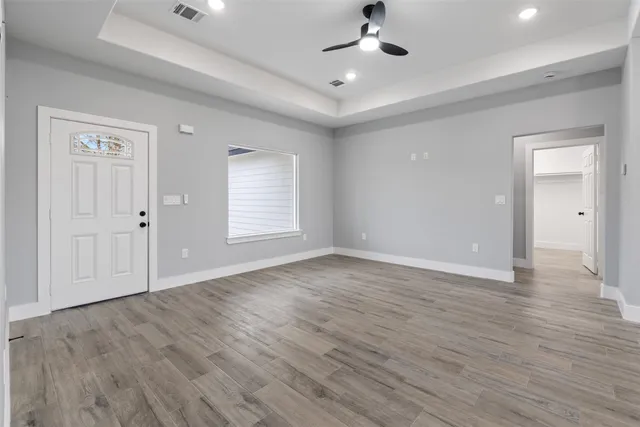 an empty room with wooden floor chandelier fan and windows