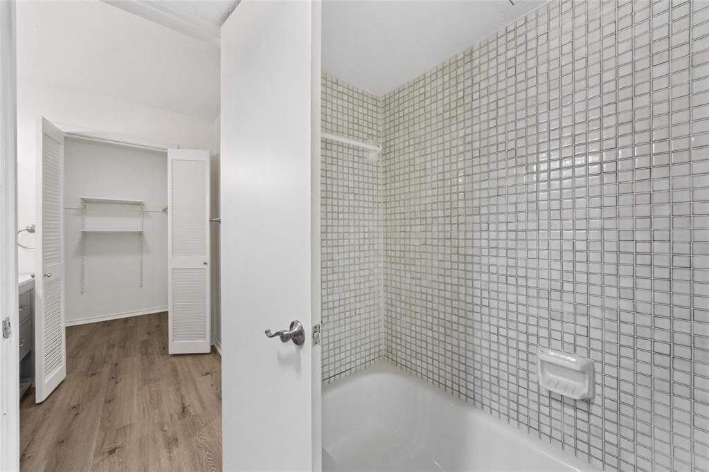 18240 Midway Road, Unit 402 Dallas, TX 75287 - Photo 19 of 29 Bathroom featuring a tiled shower surround, white bathtub, and wood-finish flooring