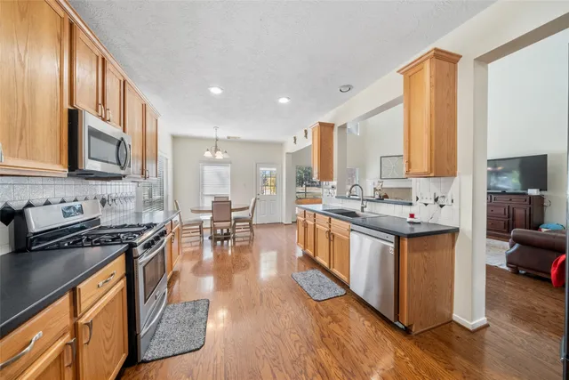 a kitchen with stainless steel appliances granite countertop a stove top oven a sink dishwasher a dining table and chairs with wooden floor