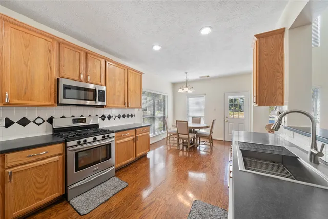 a kitchen with stainless steel appliances granite countertop a stove top oven a sink dishwasher a dining table and chairs with wooden floor