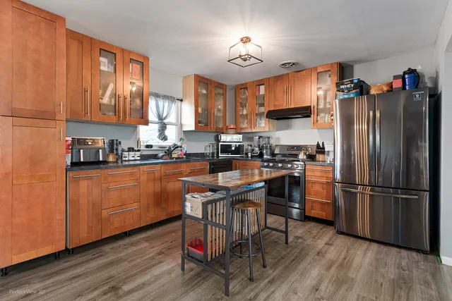 a kitchen with stainless steel appliances granite countertop a refrigerator a stove a sink dishwasher and a dining table with wooden floor