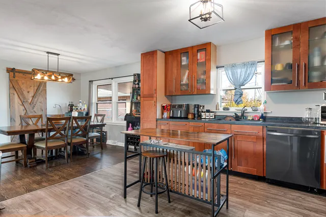 a kitchen with stainless steel appliances granite countertop a stove top oven a sink a dining table and chairs with wooden floor