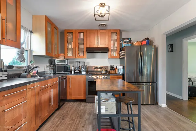 a kitchen with stainless steel appliances granite countertop a refrigerator a sink dishwasher a stove and white countertops with wooden floor