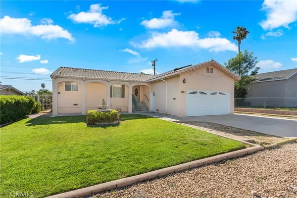 a view of a white house with a yard plants and large tree