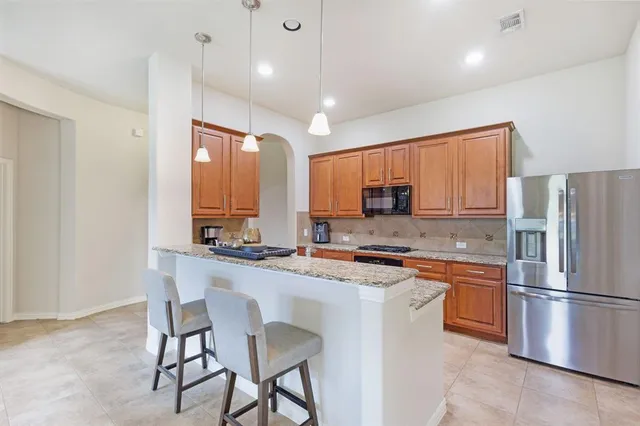 a kitchen with stainless steel appliances granite countertop a stove a sink a refrigerator white cabinets and chairs