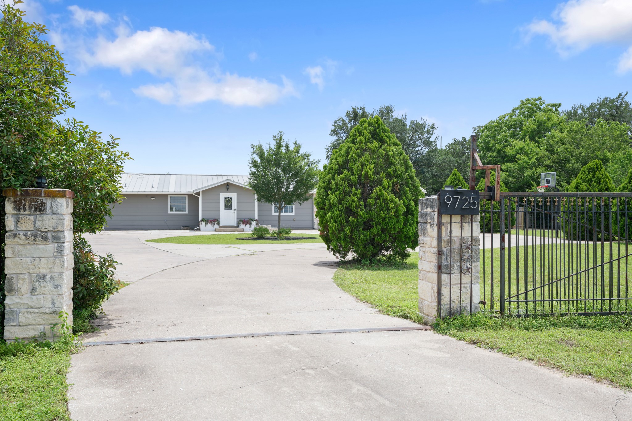 9725 Bock Road Buda, TX 78610 - Photo 2 of 32 A private driveway leads to a welcoming home, framed by mature trees and a robust gate.