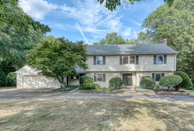 a view of a white house next to a yard with plants and trees