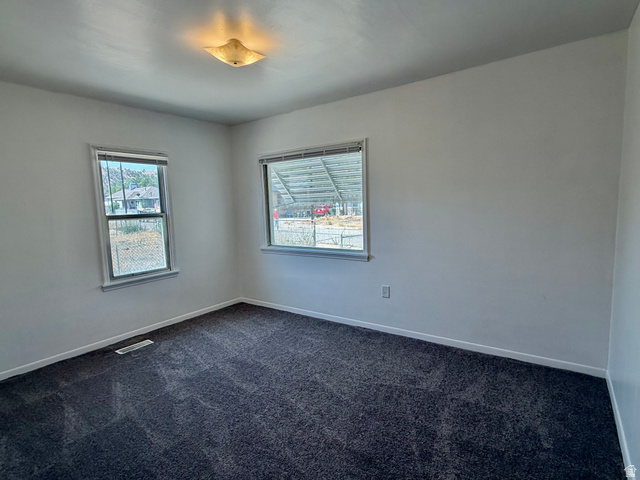 151 South Roosevelt Helper, UT 84526 - Photo 5 of 20 Room featuring two windows with horizontal blinds, neutral wall paint, dark gray carpet flooring, and a flush mount ceiling light fixture