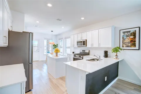 a kitchen view with stainless steel appliances a stove refrigerator sink and white cabinets with wooden floor