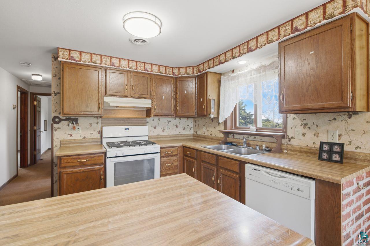 61018 Dahlstrom Road Ashland, WI 54806 - Photo 8 of 28 Kitchen featuring wood-finish cabinetry, a white gas range with overhead ventilation, a double basin stainless steel sink, and a white dishwasher