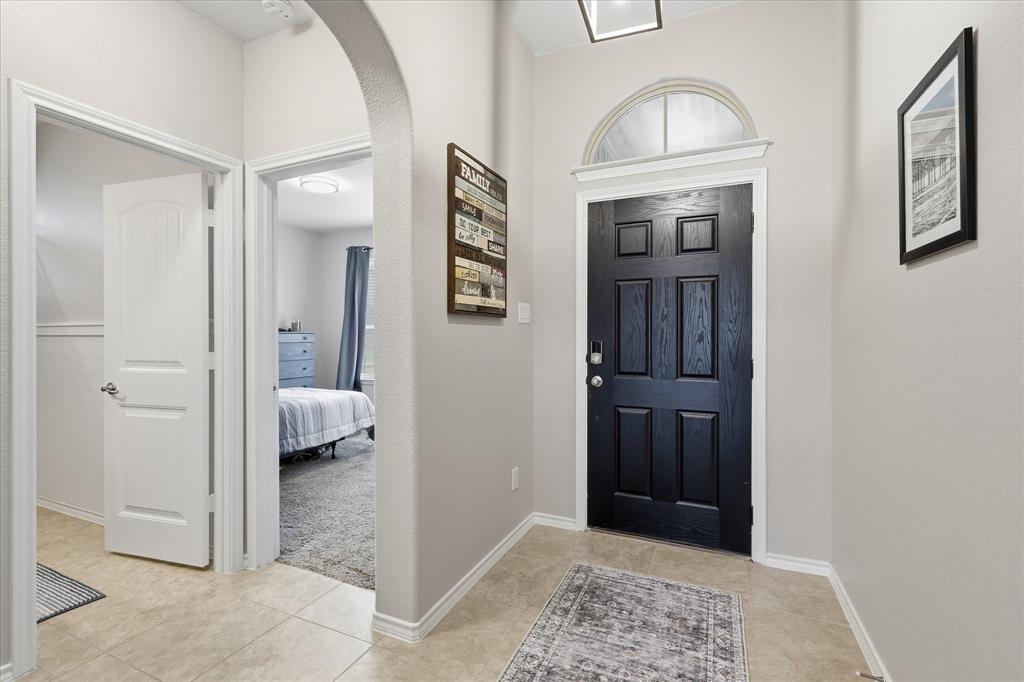 11500 Starlight Ranch Fort Worth, TX 76052 - Photo 3 of 40 Entryway featuring a black paneled door with an arched transom window, light-colored tile flooring, and a carpeted room visible through an arched doorway