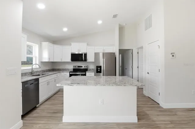 a large kitchen with stainless steel appliances granite countertop a stove a sink dishwasher a refrigerator and white cabinets with wooden floor