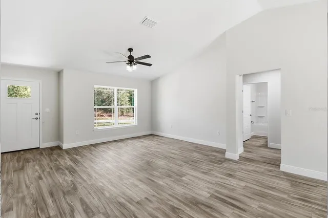 an empty room with wooden floor chandelier fan and windows