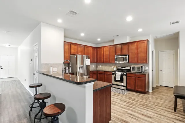 a kitchen with stainless steel appliances kitchen island granite countertop a stove refrigerator and a sink with wooden floor