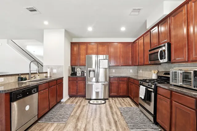 a kitchen with stainless steel appliances granite countertop a stove top oven a sink dishwasher a refrigerator and cabinets with wooden floor