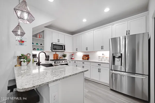 a kitchen with stainless steel appliances granite countertop a refrigerator a sink dishwasher a stove and white cabinets with wooden floor