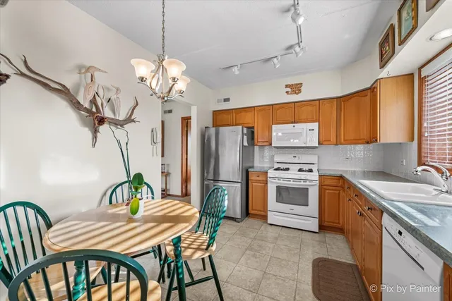 a kitchen with stainless steel appliances granite countertop a dining table chairs a refrigerator and a chandelier