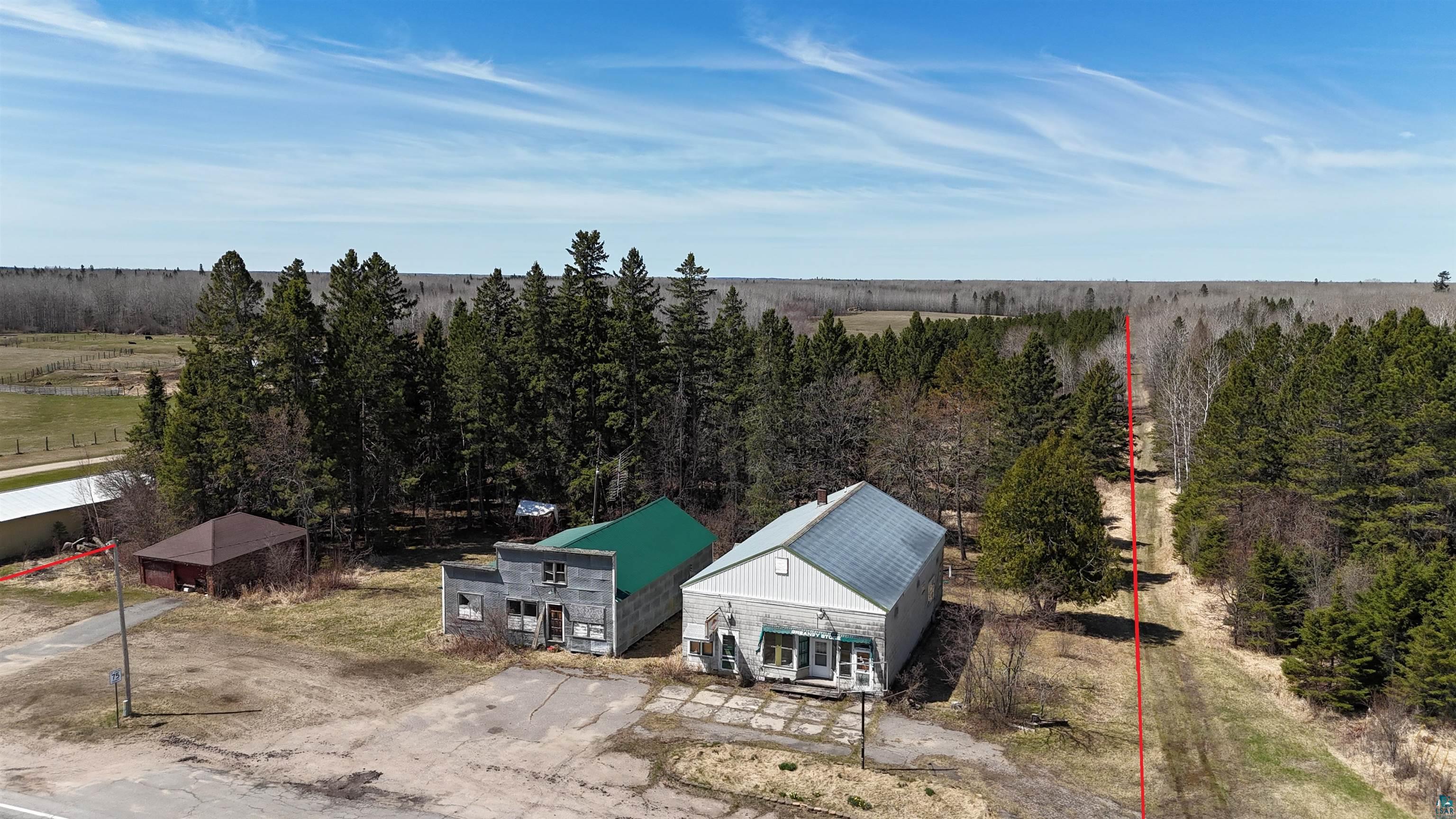3293 South Greaney Road Orr, MN 55771 - Photo 2 of 17 Commercial property featuring multiple structures, including a primary building with a green metal roof, a secondary building with a light-colored metal roof, and an additional smaller structure with a brown hip roof