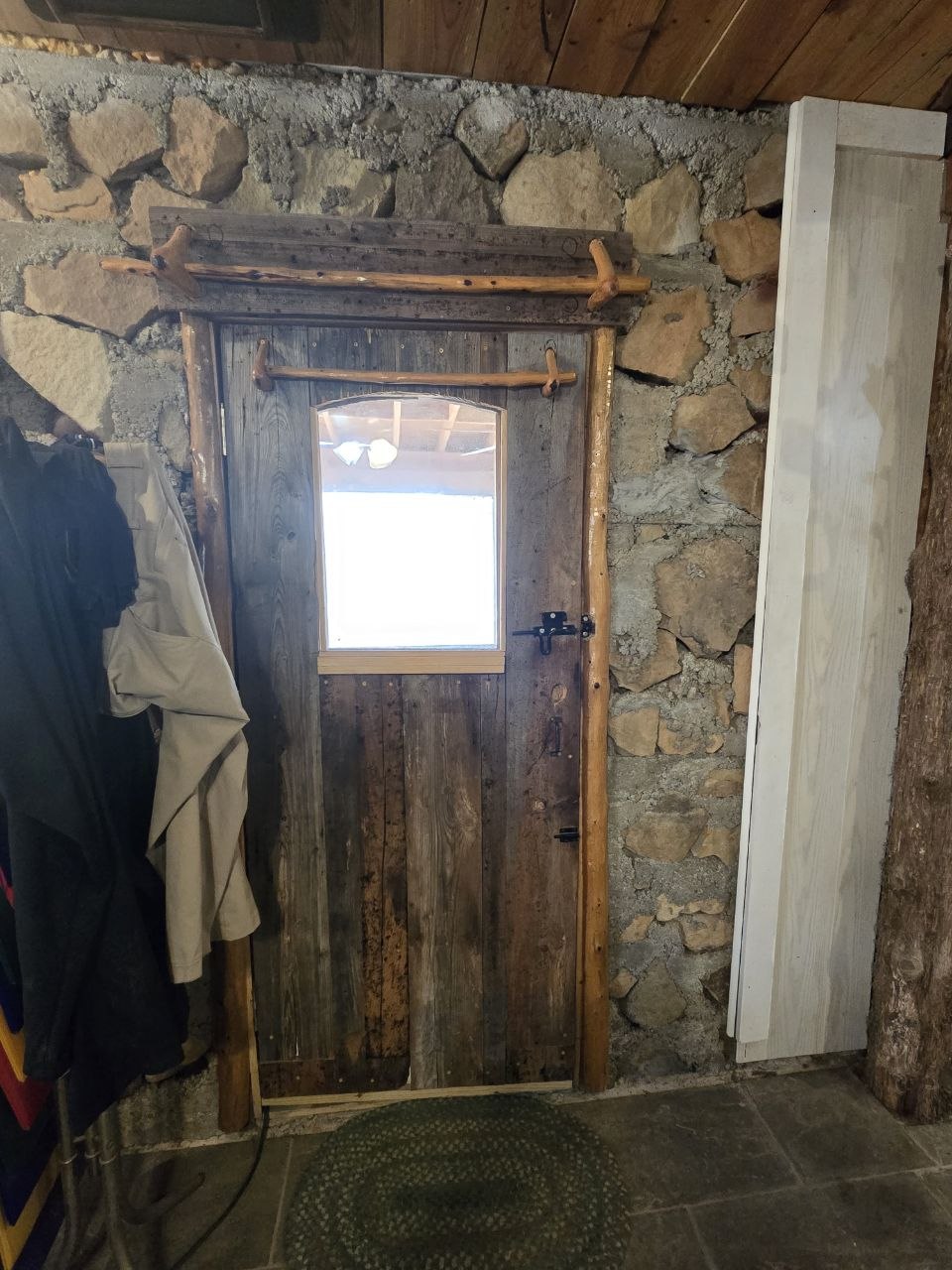 1097 Flagpole Road Clayton, OK 74536 - Photo 15 of 32 Rustic door with a clear glass window, surrounded by a natural wood frame, set into a stone wall with visible mortar, and slate tile flooring