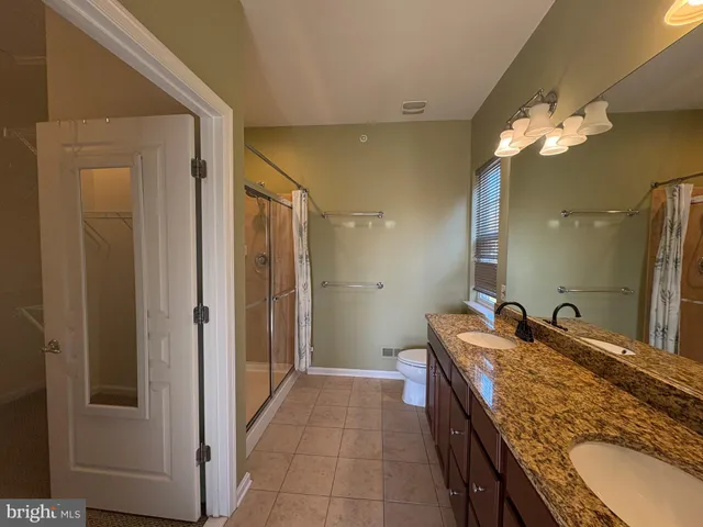 a bathroom with a granite countertop double vanity sink a mirror and a shower
