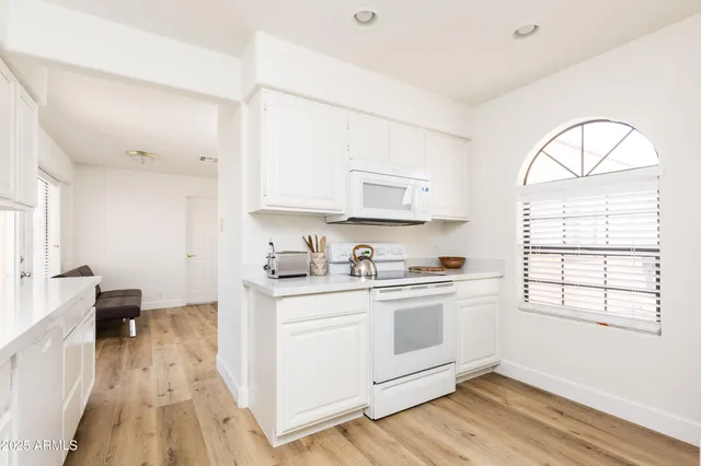 a kitchen with stainless steel appliances granite countertop a stove a sink dishwasher and white cabinets with wooden floor