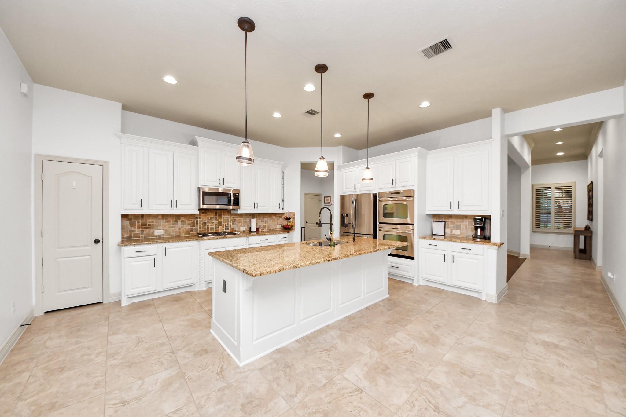 10410 Mossback Pine Road Katy, TX 77494 - Photo 9 of 34 a large white kitchen with kitchen island a sink and white cabinets