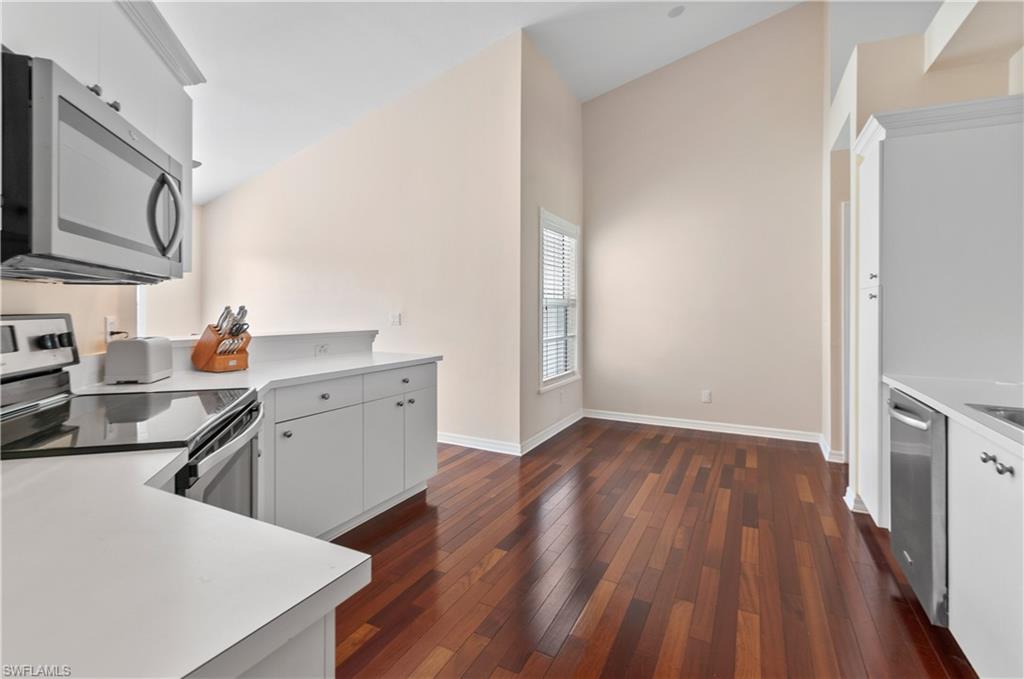 5940 Sand Wedge Lane, Unit 1407 Naples, FL 34110 - Photo 6 of 13 Kitchen featuring stainless steel appliances, light countertops, white cabinetry, dark wood-style flooring, and lofted ceiling
