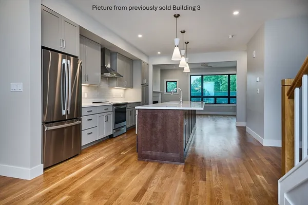 a kitchen with stainless steel appliances granite countertop a refrigerator a sink dishwasher a stove and a dining table with wooden floor