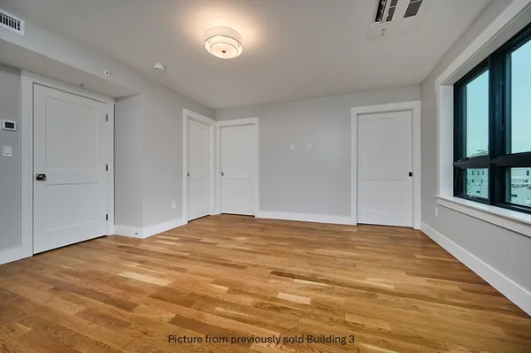 a view of an empty room with window and hardwood floor