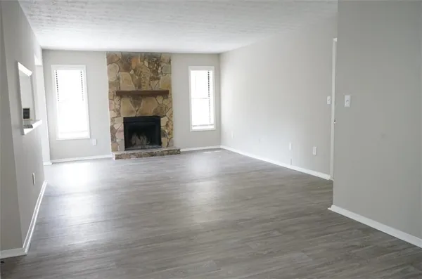 an empty room with wooden floor fireplace and windows