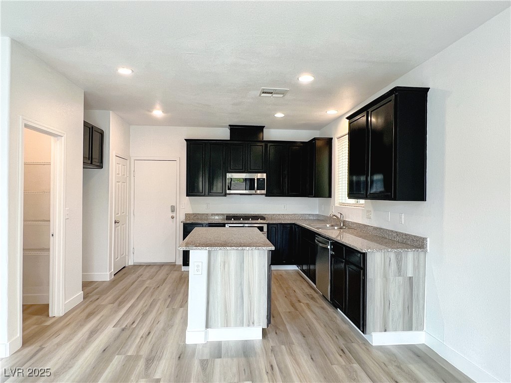 8821 Steaming Thunder Court Las Vegas, NV 89148 - Photo 10 of 31 Kitchen with dark cabinetry, light wood-type flooring, appliances with stainless steel finishes, light stone countertops, and recessed lighting