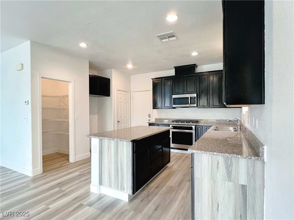 8821 Steaming Thunder Court Las Vegas, NV 89148 - Photo 11 of 31 Kitchen with dark cabinets, light stone counters, light wood finished floors, appliances with stainless steel finishes, and a center island