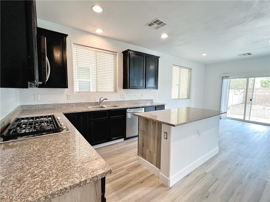 8821 Steaming Thunder Court Las Vegas, NV 89148 - Photo 12 of 31 Kitchen with dark cabinetry, light stone counters, light wood-style floors, plenty of natural light, and recessed lighting