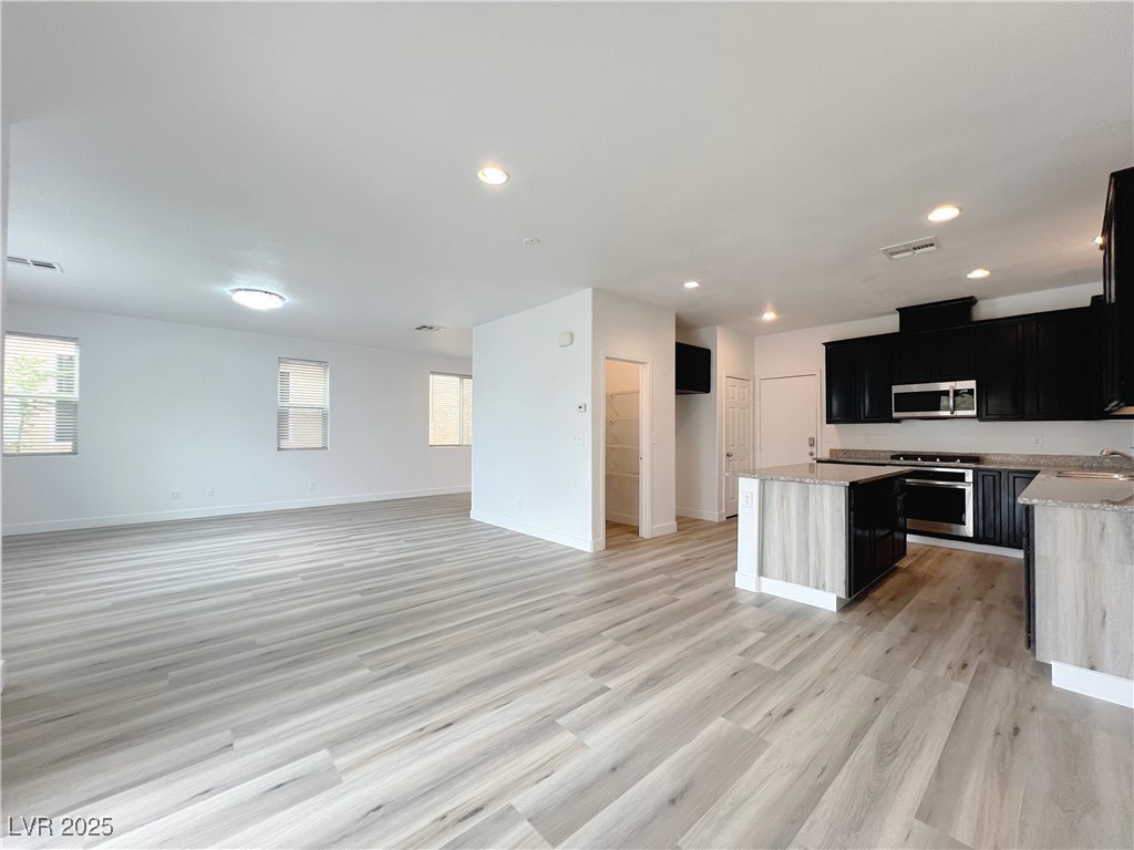 8821 Steaming Thunder Court Las Vegas, NV 89148 - Photo 31 of 31 Kitchen featuring dark cabinetry, a center island, light stone counters, light wood-type flooring, and open floor plan